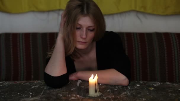Молодая грустная женщина сидит со свечой — стоковое видео