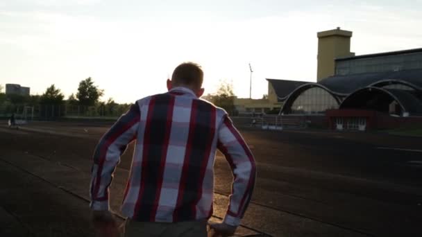 O tipo está a atravessar o estádio ao pôr-do-sol. — Vídeo de Stock