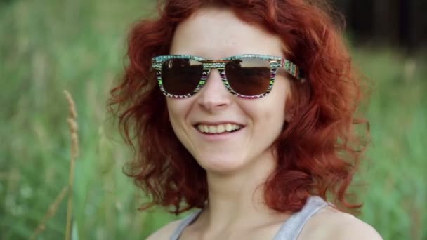 Femme en lunettes de soleil souriant contre l'herbe verte — Video