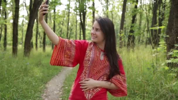 Жінка в червоній сорочці робить селфі в парку — стокове відео