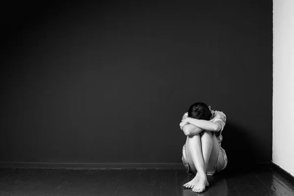 Sad woman sitting in the corner of a room — Stock Photo, Image