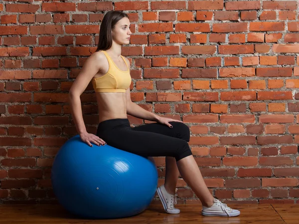 Mujer joven sentada en la pelota, sobre el fondo de la pared de ladrillo — Foto de Stock