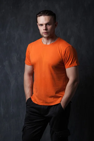 Hombre fuerte con una camisa naranja metida las manos en los bolsillos —  Fotos de Stock