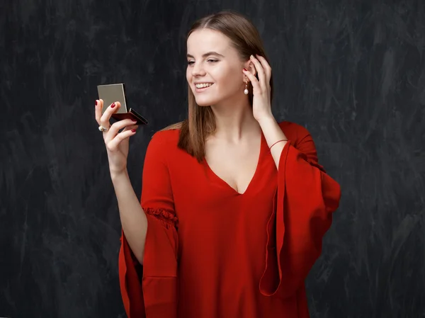 Mujer joven en vestido rojo está mirando en un pequeño espejo de bolsillo . — Foto de Stock