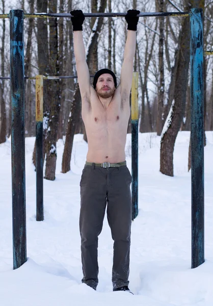 Fitness model doing pull-ups in winter park on a background of