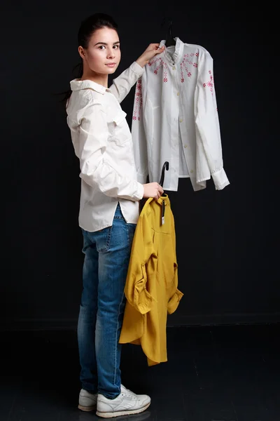 Young brunette woman choosing one  shirt of two — Stock Photo, Image