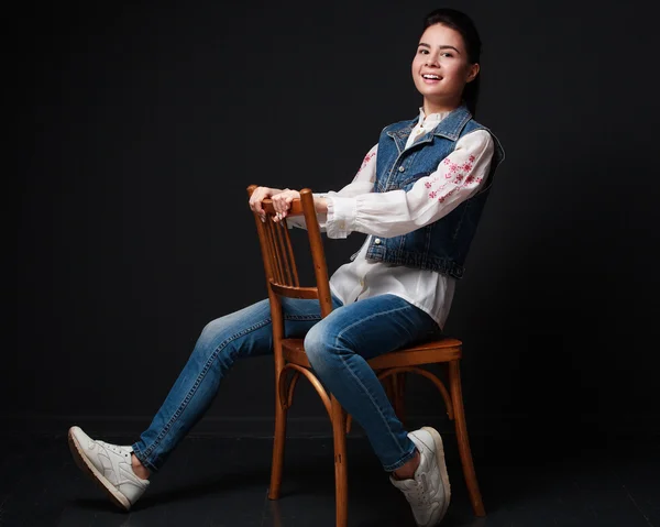 Playful young  brunette woman in jeans suit sitting on the chair
