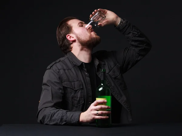 Ung man dricker alkohol från ett vinglas, flaska på t — Stockfoto