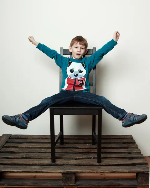 Kleiner lustiger Junge sitzt auf dem Stuhl, streichelt, narrt — Stockfoto