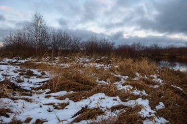 Sonbaharda göl kenarındaki tarlada kuru çimenler ve ilk kar. Manzara Görünümü.