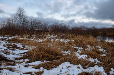 Sonbaharda göl kenarındaki tarlada kuru çimenler ve ilk kar. Manzara Görünümü.
