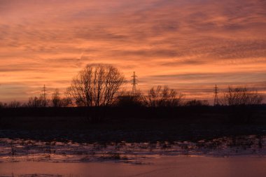 Sonbaharın sonlarında günbatımına karşı tarlalardaki yüksek voltajlı elektrik hatlarının direkleri.