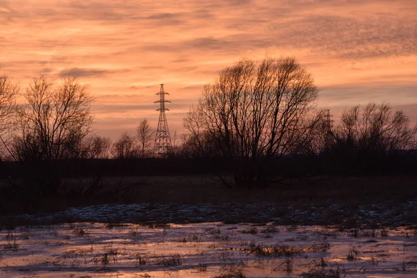 Pillars of a high-voltage power line in the fields in late autumn against the sunset