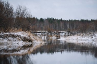 Sonbaharın sonlarında nehir kenarındaki ağaçlar kuru çimenler ve ilk karla kaplı. Manzara Görünümü.