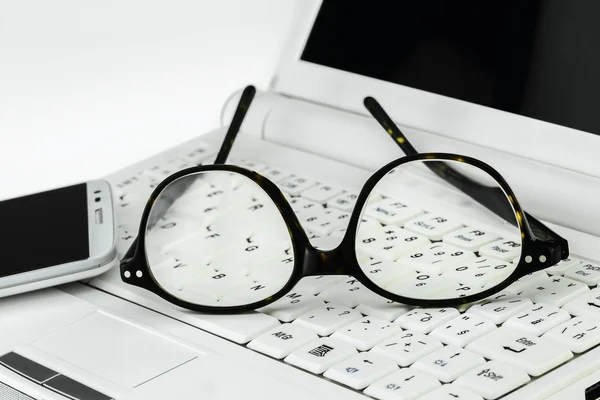 Eyeglasses  and cell phone on a small laptop — Stock Photo, Image