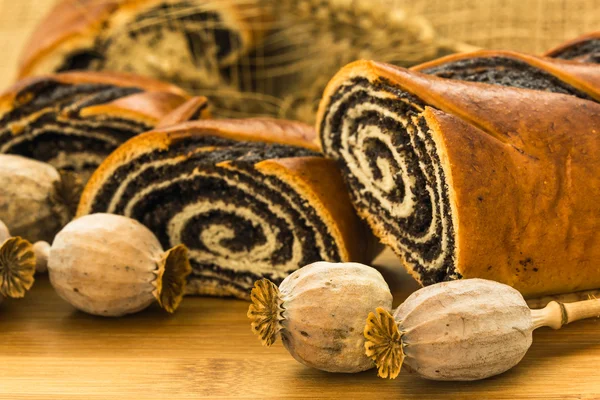 Poppys' heads in the foreground and poppy-seed strudels with whe — Stock Photo, Image