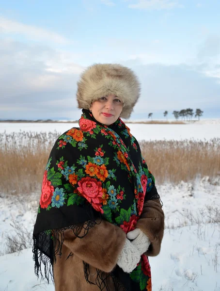 Portrait de la femme d'âge moyen dans une casquette de fourrure et un châle coloré contre le lac d'hiver — Photo