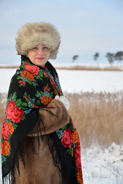 The portrait of the woman of middle age in a fur cap and a colorful shawl costs against the winter lake — Stock Photo, Image