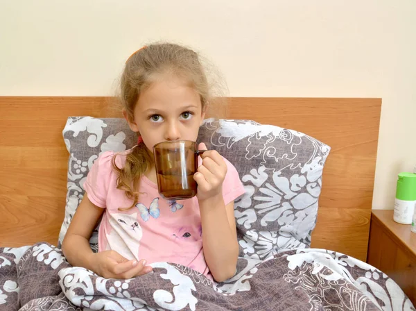 病気の女の子は薬を飲むマグカップから水で ベッドに座って — ストック写真