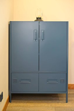 Odada bacakları üzerinde mavi metal bir dolap duruyor.