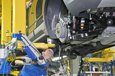 KALININGRAD, RUSSIA - 16 Eylül 2014: Genç bir işçi pnömatik tornavida kullanarak arabanın altına bir parça ekler. Bir otomobil fabrikasının montaj hattı