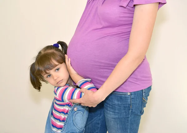 La petite fille embrasse les mains d'un estomac de mère enceinte — Photo