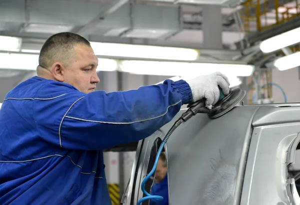 The worker grinds a car body. Automobile plant — Stock Photo, Image