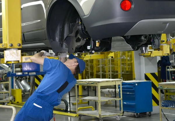 De werknemer corrigeert een detail aan de onderkant van de auto. vergadering transportband o — Stockfoto