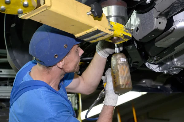 The worker fixes a detail to the car bottom. Assembly conveyor o — Stock Photo, Image