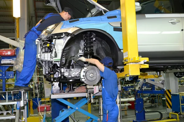 Les travailleurs installent le moteur sur la voiture. Convoyeur d'assemblage de l'automobile — Photo