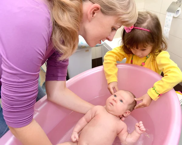 Das dreijährige Mädchen hilft der Mutter, das Baby in rosa zu baden — Stockfoto