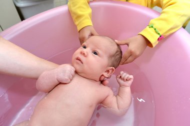 Küçük kız anne bebek banyo için yardımcı olur.