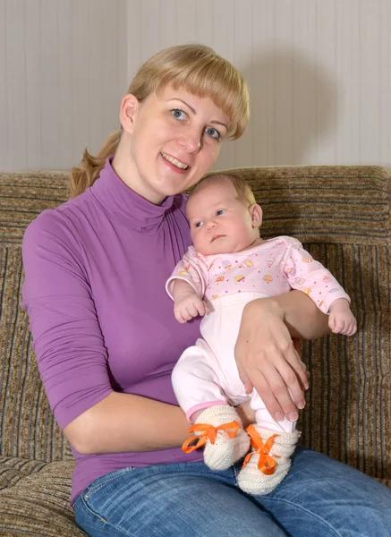 Die junge Frau sitzt auf einem Sofa mit dem Baby an den Händen — Stockfoto