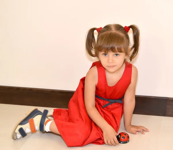 La bambina in un vestito rosso si siede su un piano con un giocattolo — Foto Stock