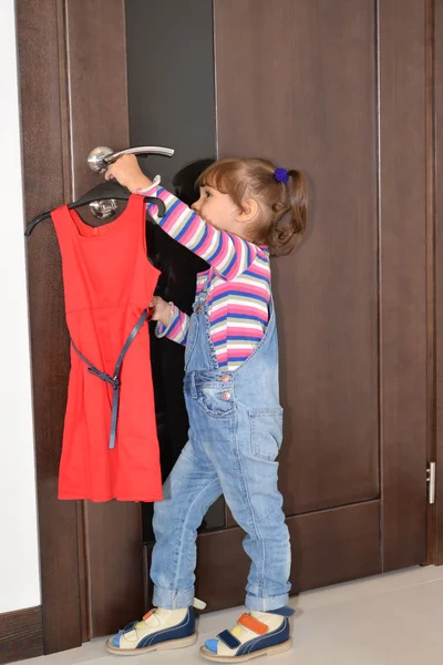 The three-year-old girl takes off from the door handle a beautif — Stock Photo, Image