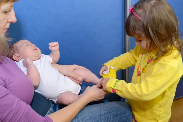 Das dreijährige Mädchen kleidet Stiefel an die Füße des Babys. clo — Stockfoto