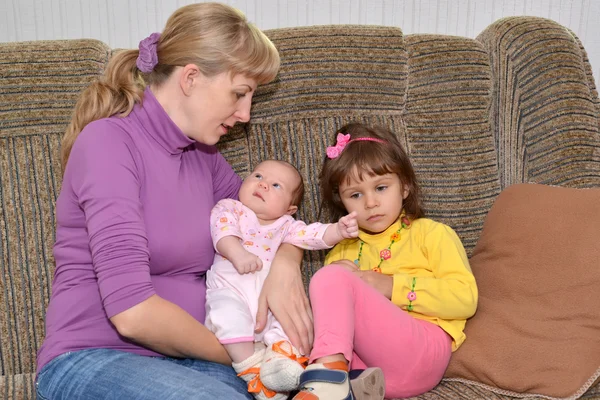 Mladé ženy s dvěma malými dětmi sedět na pohovce — Stock fotografie