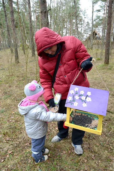 The young man with the daughter put grains in a birds feeder — Stock Photo, Image