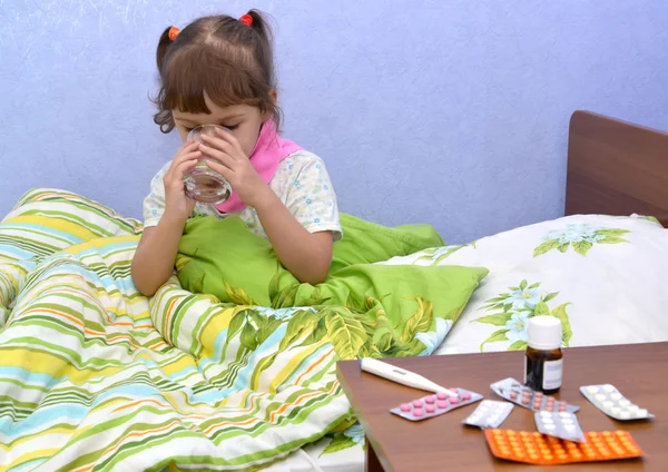 La niña enferma se sienta en una cama y bebe agua de un vaso. — Foto de Stock