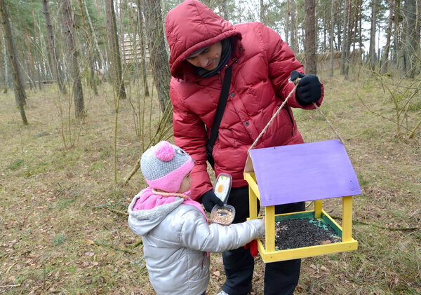 The young man with the daughter put grains in a birds feeder