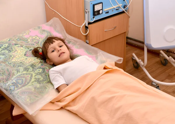 Маленькая больная девочка лежит на диване в физиотерапевтическом кабинете — стоковое фото
