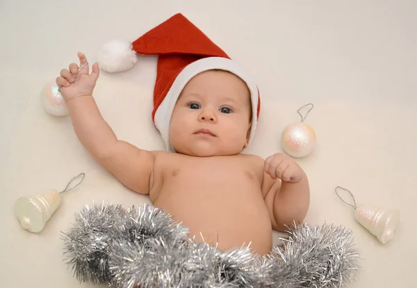 The baby in Santa Claus's cap with Christmas tree decorations on Stock Picture