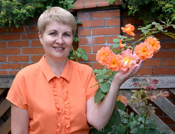 The cheerful woman of average years shows a rose hand in a garde — Stock Photo, Image