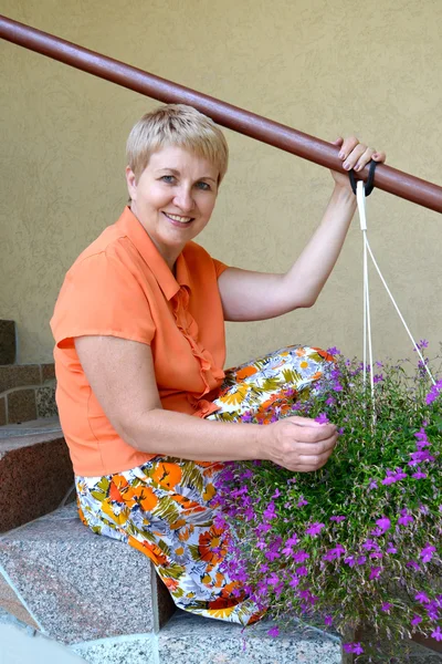 Die fröhliche Frau durchschnittlichen Alters sitzt auf einer Leiter mit dekorativen — Stockfoto
