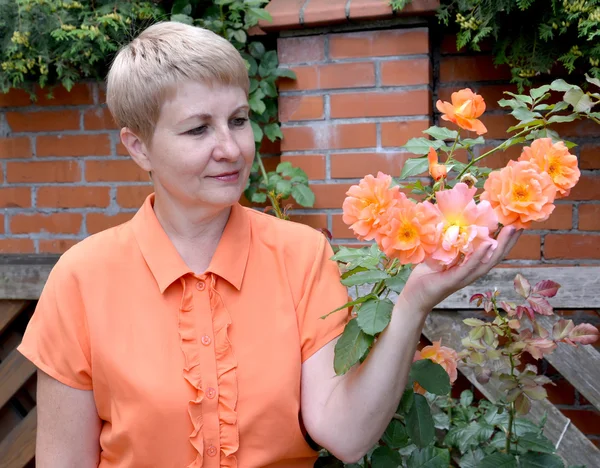 The cheerful woman of average years shows a rose hand in a garde — Stock Photo, Image