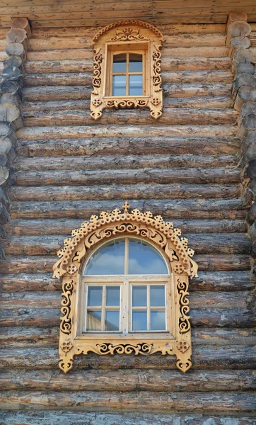 Deux fenêtres avec des plates-bandes sculptées en bois sur un mur à bois — Photo