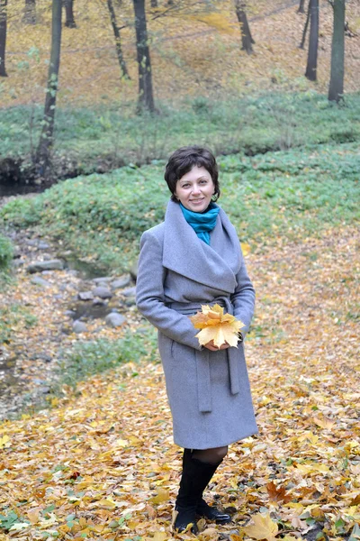 The woman of average years stands near a stream in autumn park