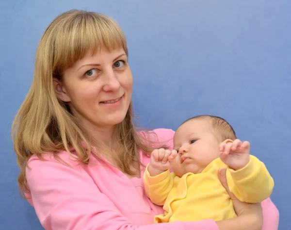 Die glückliche junge Frau mit dem Baby auf blauem Hintergrund — Stockfoto