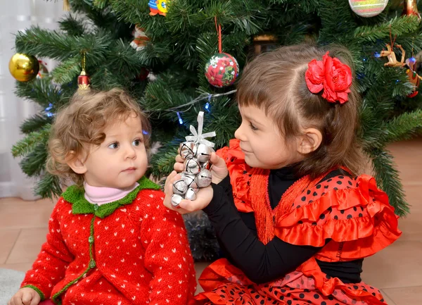 Het kleine meisje in het Spaanse pak toont aan de een-jaar-oude liittle zus een speelgoed over een nieuwe jaar boom — Stockfoto