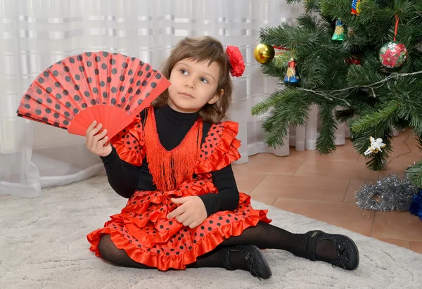 A menina no terno espanhol com um torcedor senta-se sobre uma árvore de Ano Novo — Fotografia de Stock